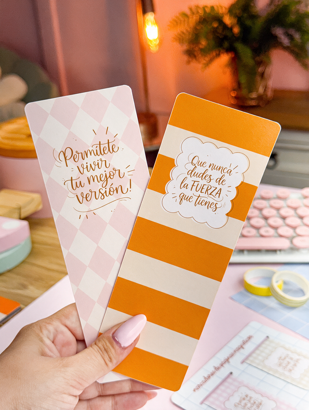 Marcapáginas bonitos con frases motivadoras, uno de rombos rosa pastel y otro de rayas naranjas, sostenidos en la mano