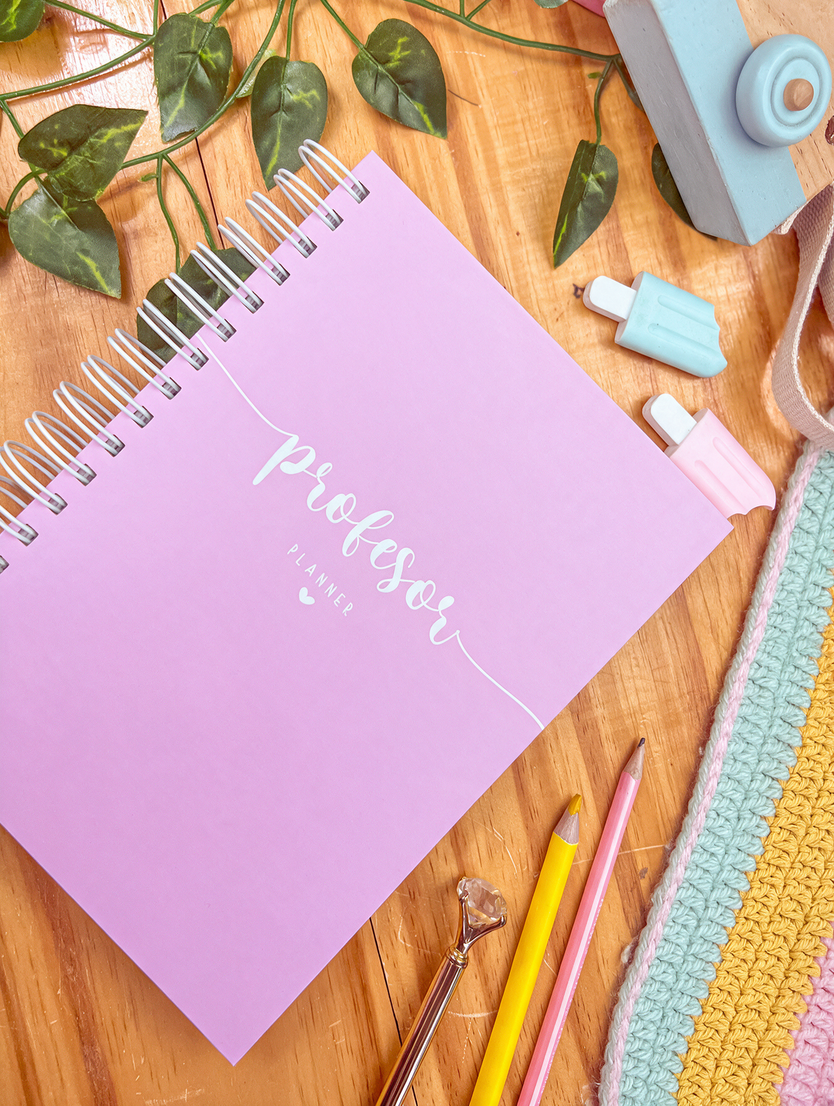 Agenda docente de anillas con portada rosa y la palabra «profesor planner» en blanco, sobre una mesa de madera con lápices