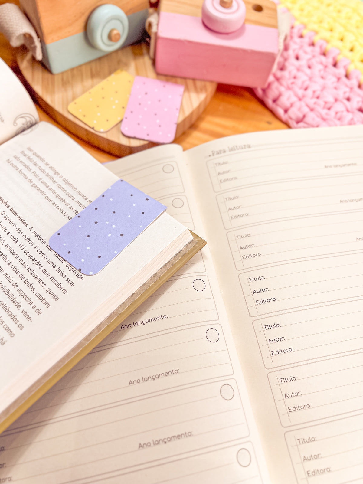 Marcapáginas magnético lila con puntos sujeto al borde de las páginas de un libro abierto, junto a otros dos marcapáginas, uno amarillo y otro rosa