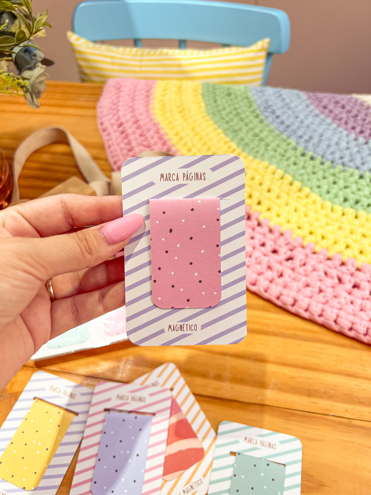 Marcapáginas magnético rosa con puntos oscuros y blancos sobre cartulina de rayas lilas, sostenido en la mano