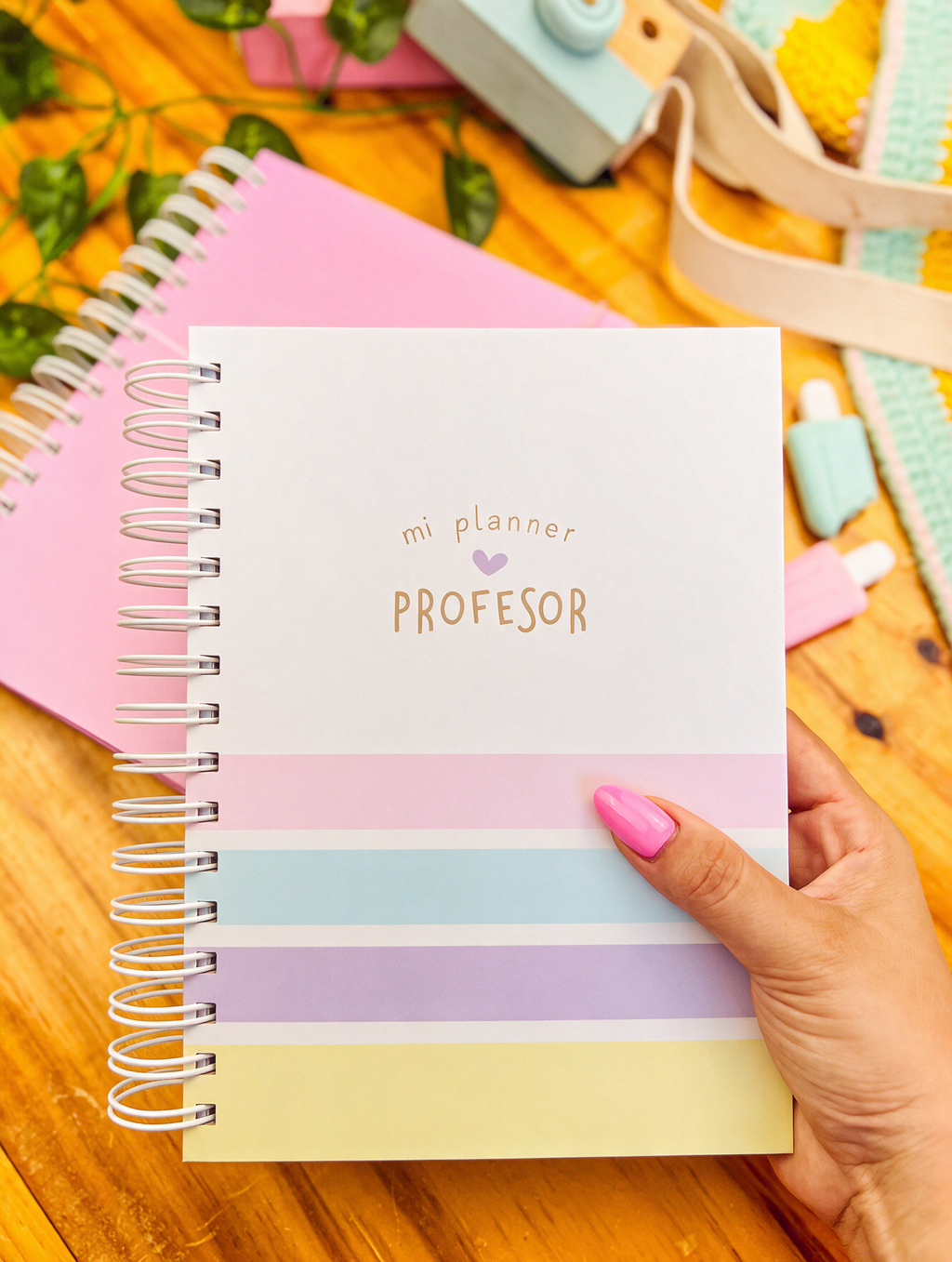 Planificador docente de anillas con portada «mi planner profesor» y rayas pastel rosa, azul, lila y amarillo, sostenido en la mano