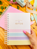 Planificador docente de anillas con portada «mi planner profesor» y rayas pastel rosa, azul, lila y amarillo, sostenido en la mano